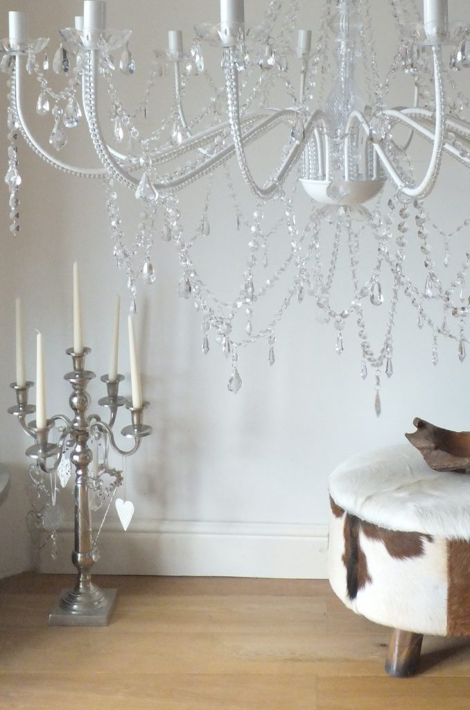 white and crystal chandelier with a tall silver candelabra covered in hanging hearts in the background for Cotswold weddings