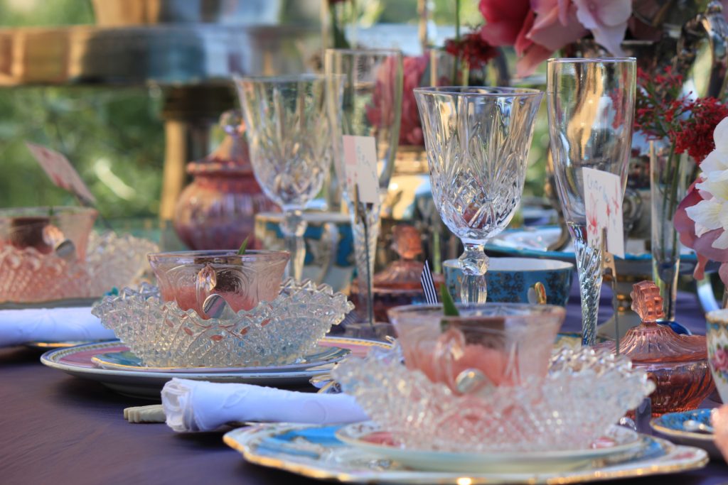 Close up of three vintage tableware set ups of white charger plates then a side plate on top and a vintage glass posy vase on top and silver vintage cutlery of starter main and desserts set each side and cut crystal wine and champagne glasses and saucers all in white, pink, blue and lilac for hire