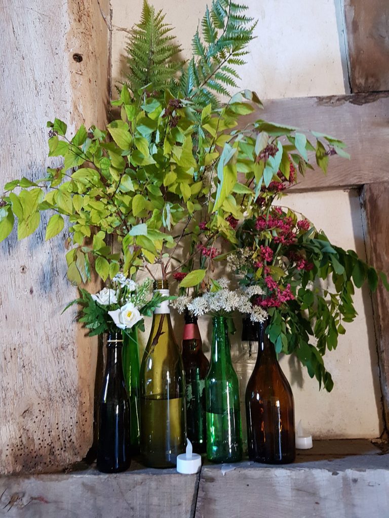 green glass bottles as vases with fresh foliage and wild flowers available to hire for weddings and events