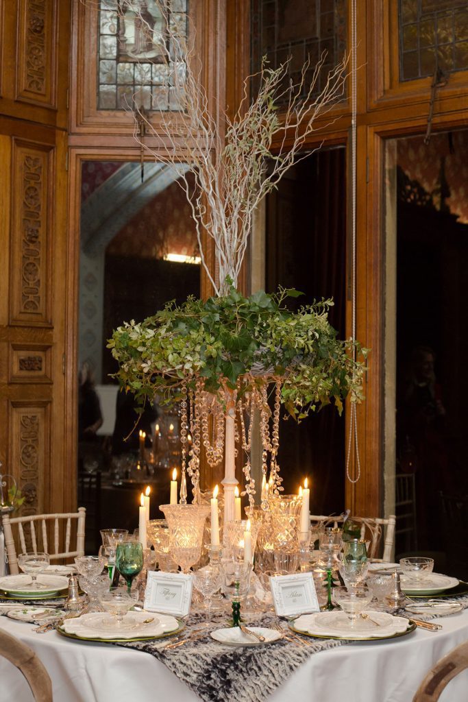 Fresh foliage wreath with ivy and hanging crystal chains centrepiece, with vintage glass vases and vintage glass candlestick and tealight holders and vintage wine, champagne and water glasses on a faux fur tablecloth to hire