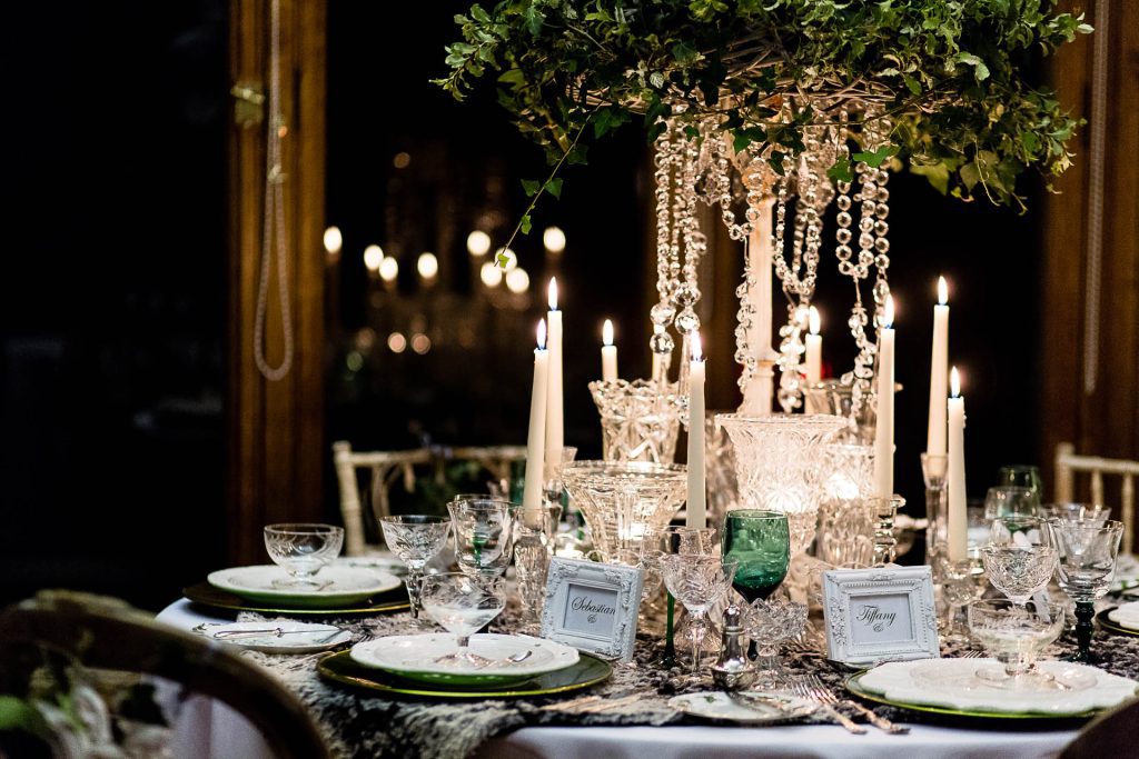 Fresh foliage wreath with ivy and hanging crystal chains centrepiece, with vintage glass vases and vintage glass candlestick and tealight holders and vintage wine, champagne and water glasses on a faux fur tablecloth to hire