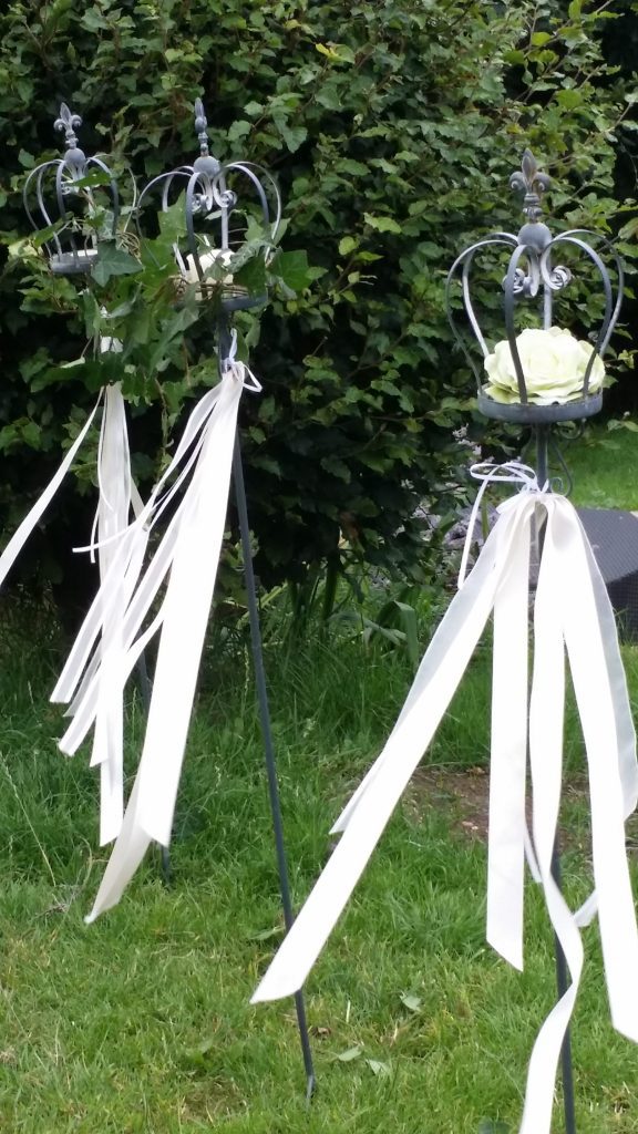 Three silver stakes with a crown top and white rose sat in the crown with white ribbon tied round the pole blowing in the wind.