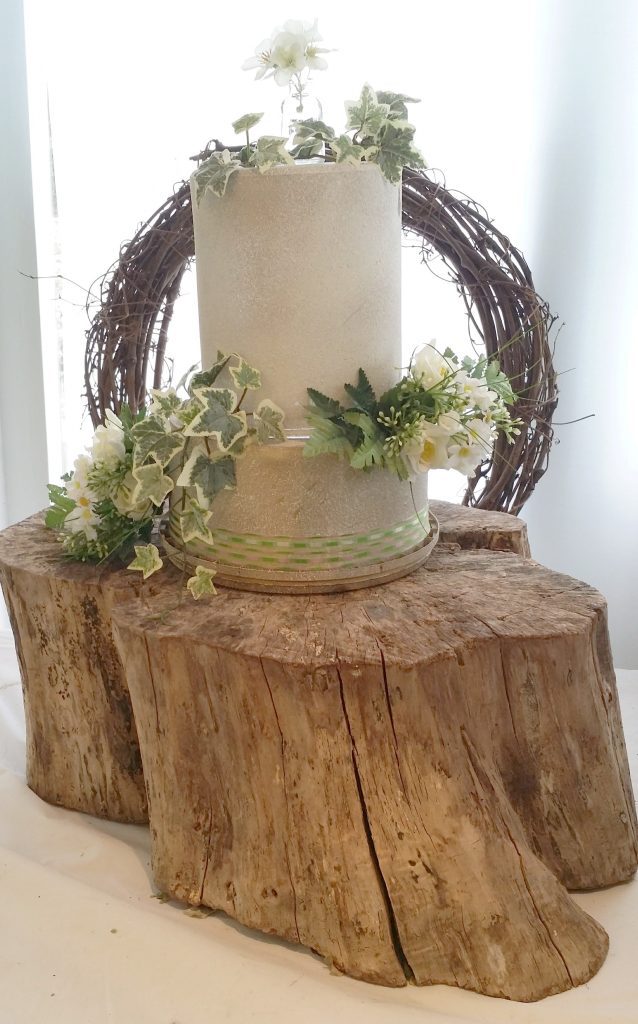 woodland tree stump cake stand wrapped with ivy and wicker wreath back drop for wedding cakes available to hire for weddings and events