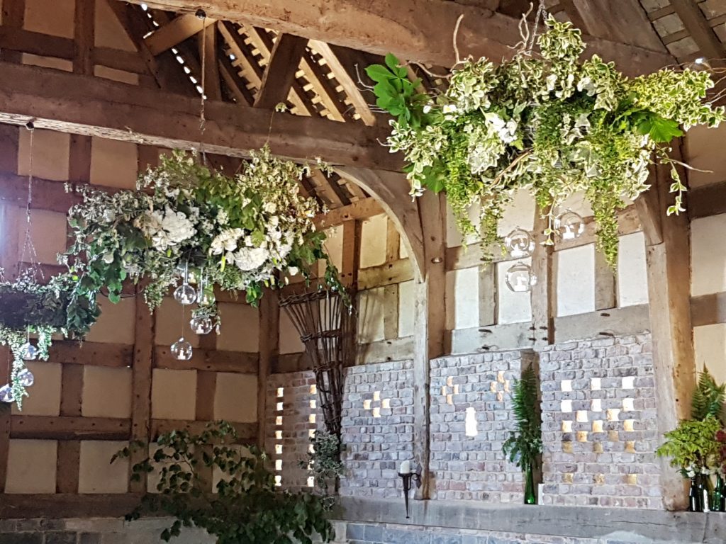 wooden wicker hanging wreath with ivy , faux flowers and glass baubles. green glass bottles in the alcoves around the room all available to hire for wedding and events and film at Frampton Barn wedding venue